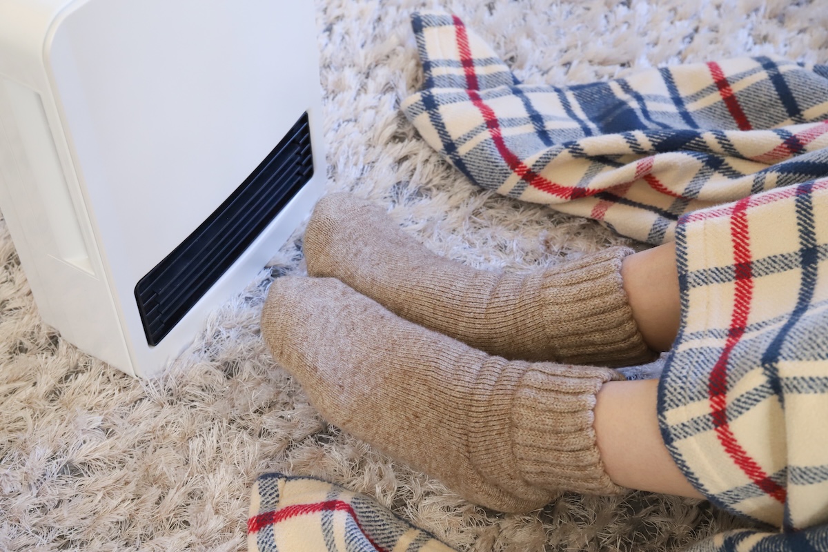 ファンヒーターの前で毛糸の靴下を履き、ブランケットにくるまって温まる足元。