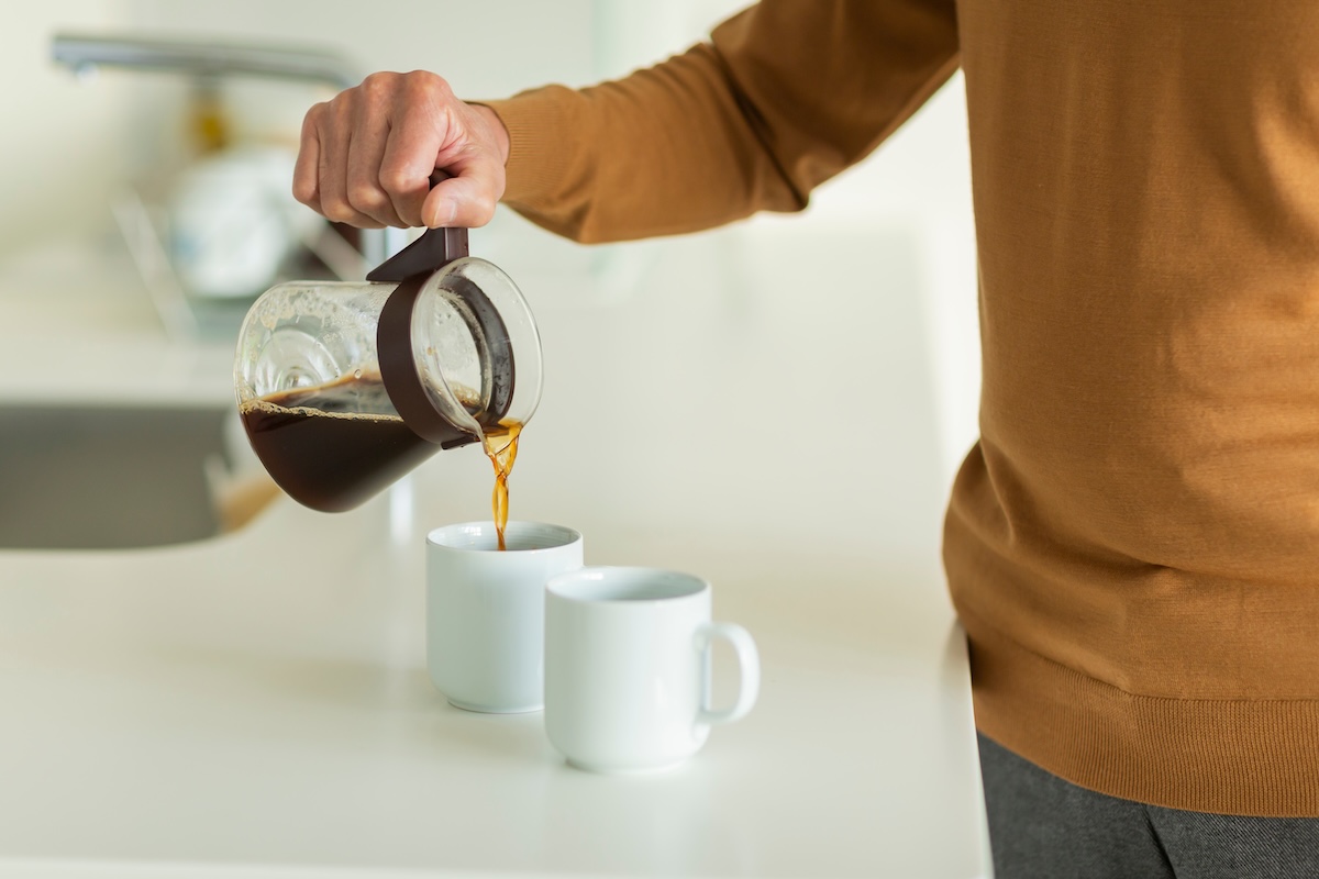 ガラス製のコーヒーポットから白いマグカップにコーヒーを注いでいる様子