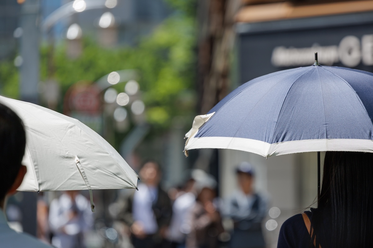 強い日差しを避けるために日傘を差して歩く街中の人々