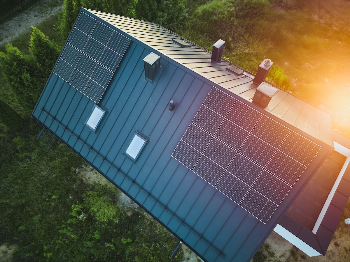 住宅の屋根に設置された太陽光パネルと夕日、再生可能エネルギーを活用する省エネ住宅の象徴