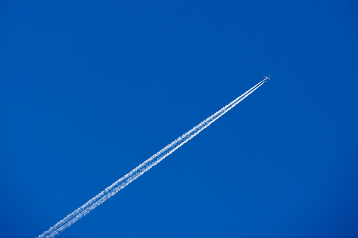 青空を横切る飛行機と長く伸びる飛行機雲、大気中へのCO2排出を連想させる景観