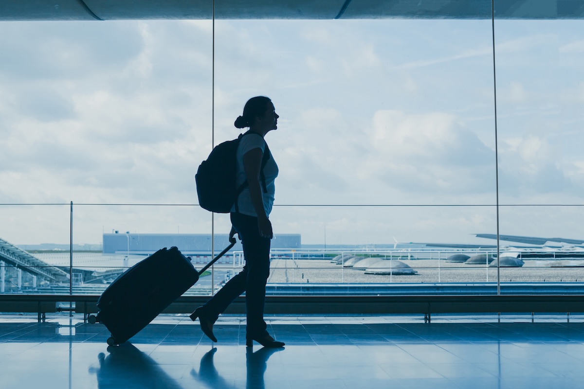 空港でスーツケースを引いて歩く旅行者のシルエット、航空機による移動とCO2排出のイメージ