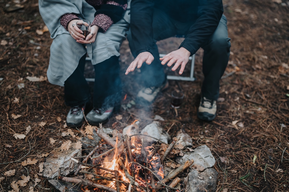 森の中で焚き火を囲み、手を温める人々。アウトドアでの火の扱いと安全対策をイメージした写真。