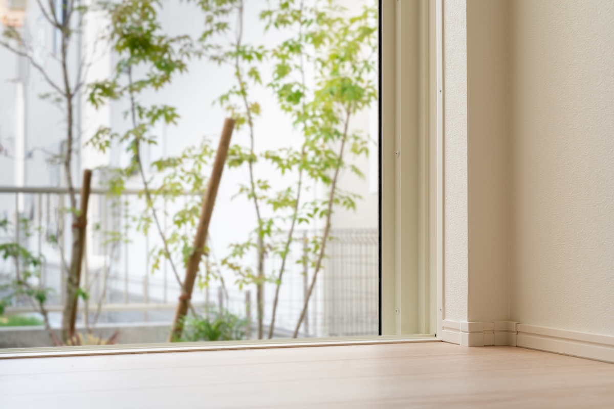 窓の外に緑が見える明るい室内。自然光を活かした省エネ住宅やエコな暮らしをイメージ。