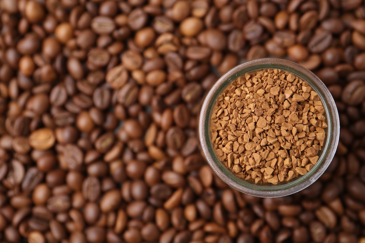 コーヒー豆の上に置かれた瓶入りインスタントコーヒー。焙煎豆との質感の違いが分かる。