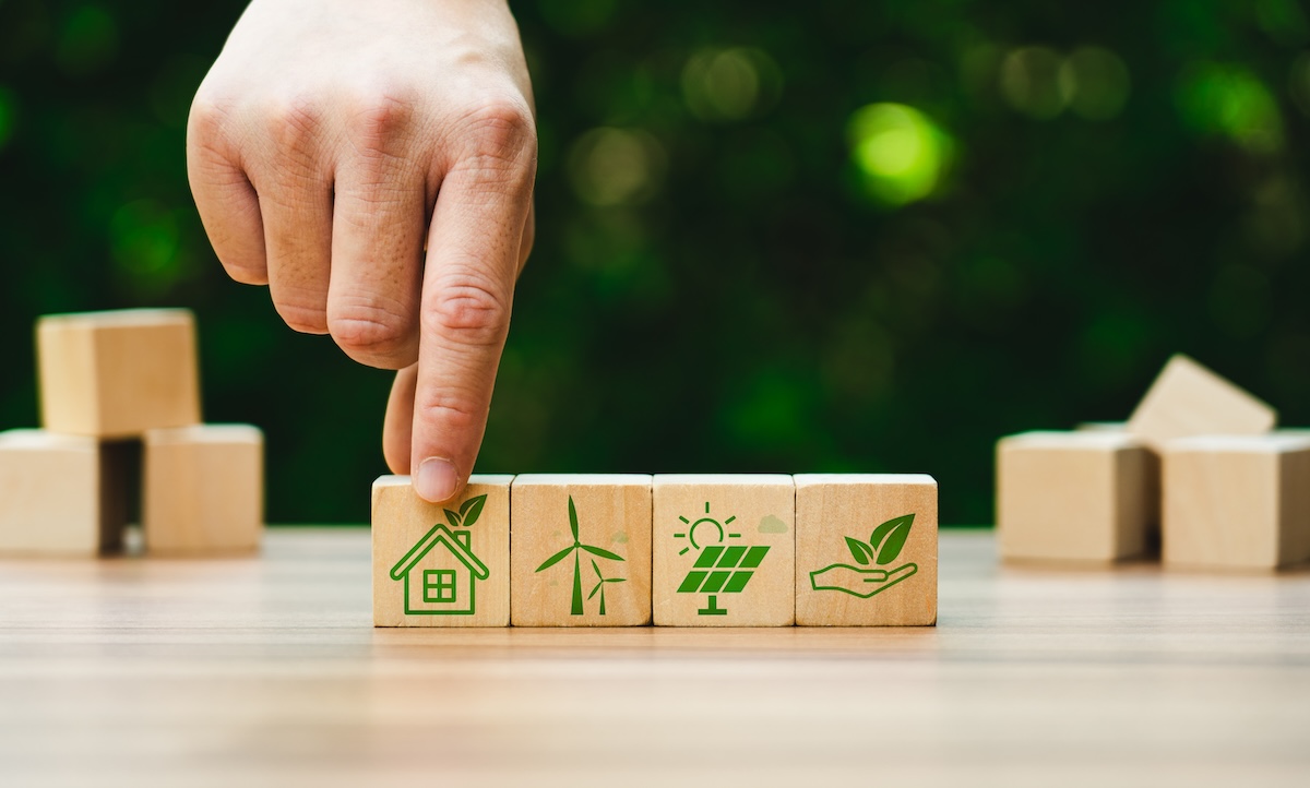 木製ブロックに描かれた再生可能エネルギーのアイコン。エコ住宅・風力発電・太陽光発電・自然保護を象徴するイメージ。