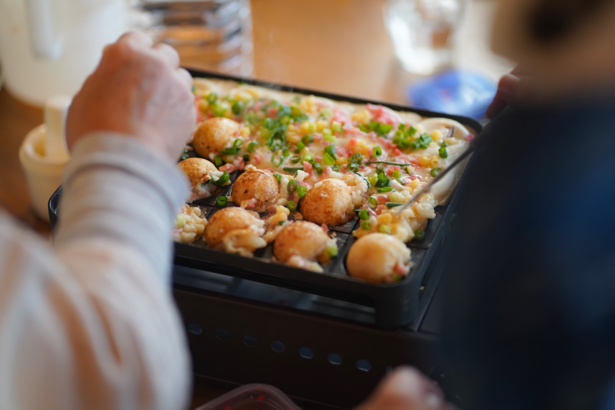 ホットプレートでたこ焼きを焼く人の手元。家庭で楽しむ電気調理や省エネクッキングのイメージ。