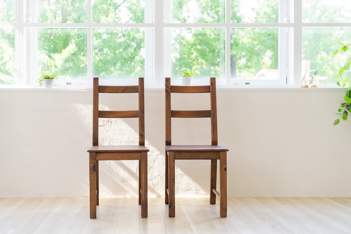 日差しが差し込む窓際に並んだ2脚の木製椅子。シンプルで温かみのある暮らしのイメージ。