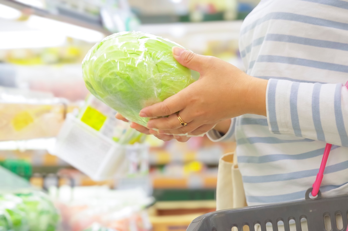 スーパーでレタスを手に取って選ぶ人。食品価格の比較や節約を意識した買い物の様子。