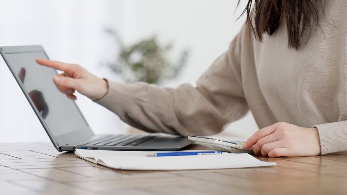 ノートパソコンと電卓で家計をチェックする女性。物価高対策や節約を意識した家計管理。