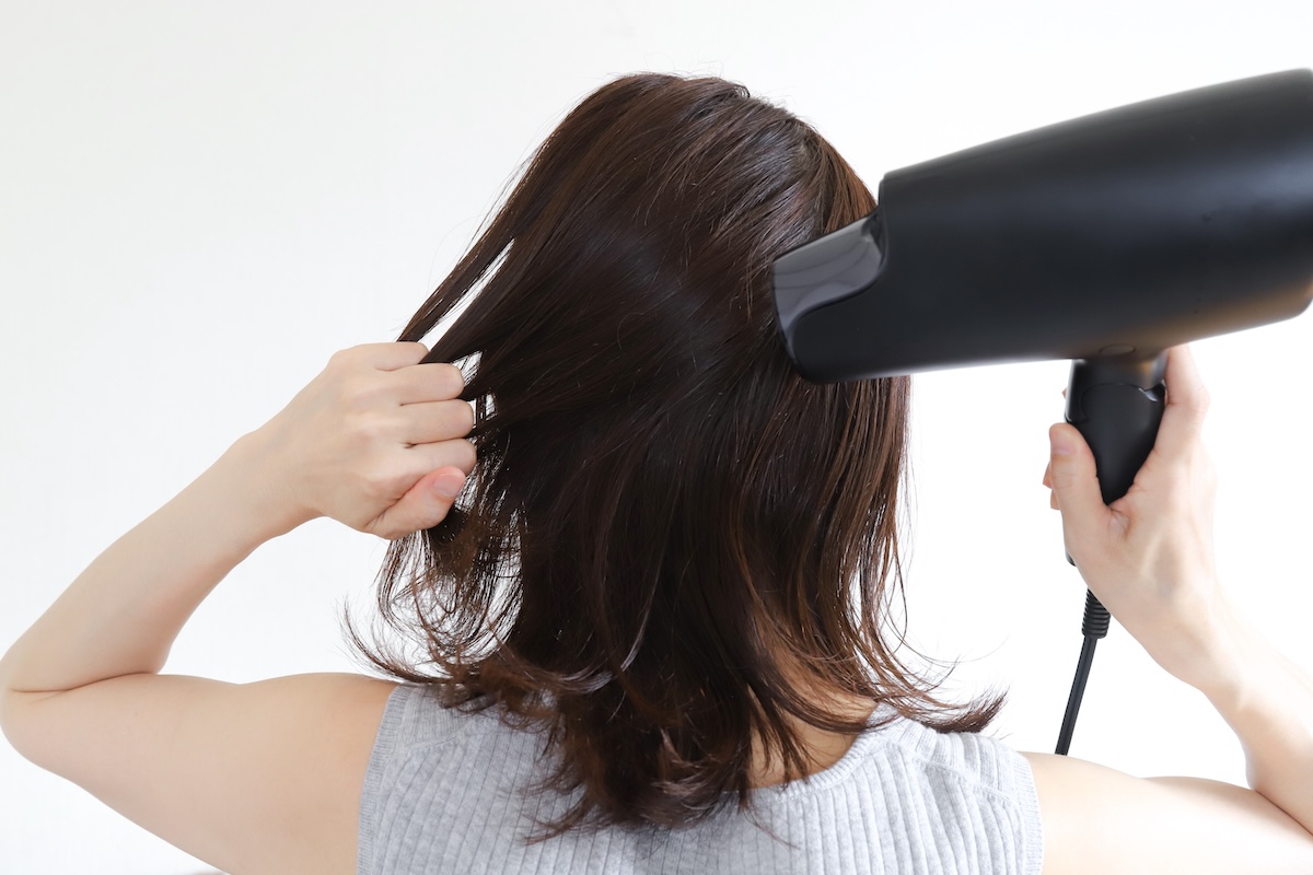 ドライヤーで髪を乾かす女性。