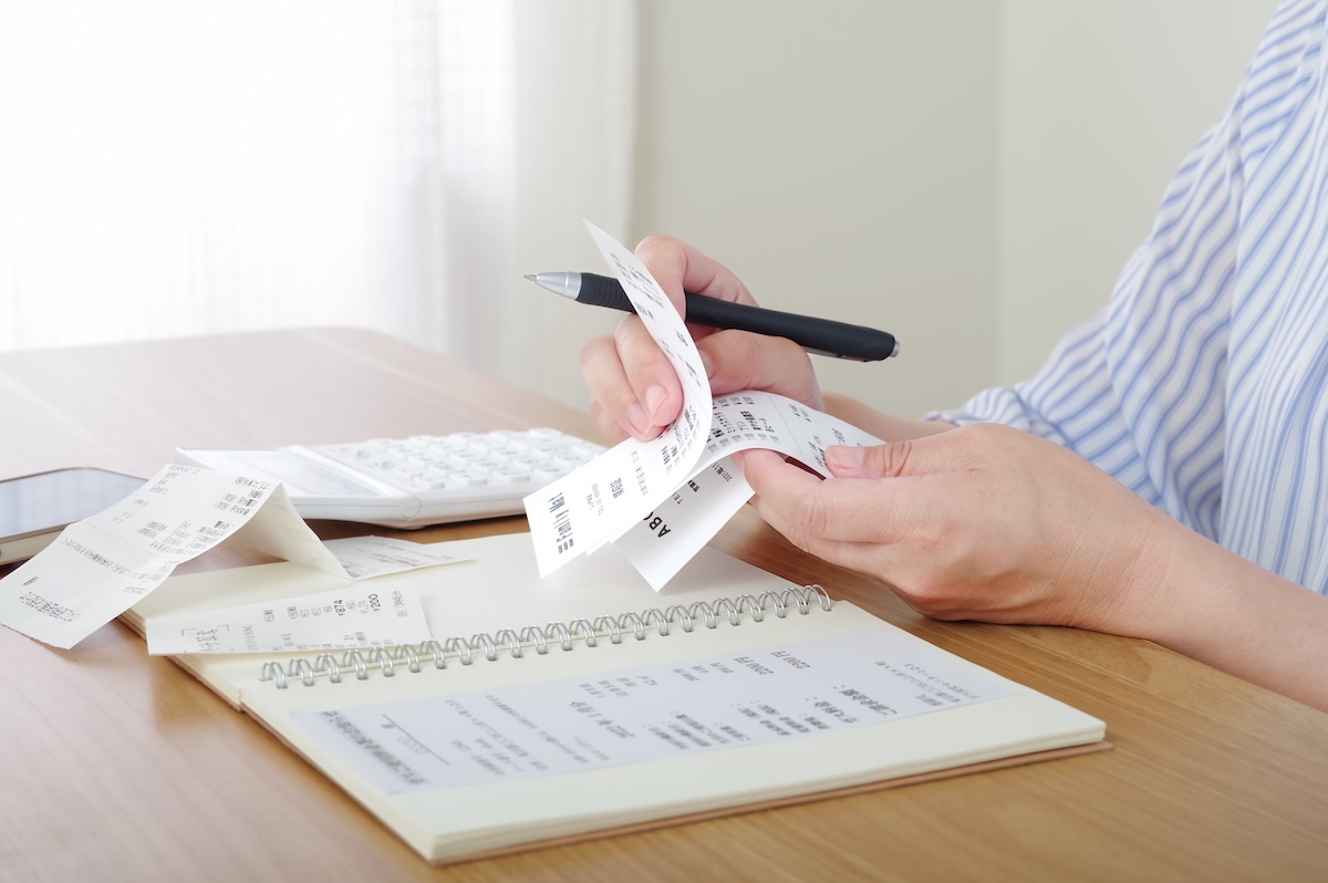 レシートと家計簿を見ながら支出を整理する手元。家計管理や節約を意識した生活をイメージした写真。