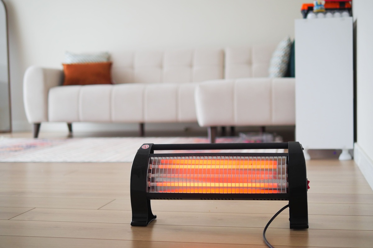 リビングの床に置かれ、オレンジ色に発光するハロゲンヒーター。冬場の暖房器具と電気代の関係を示す写真。