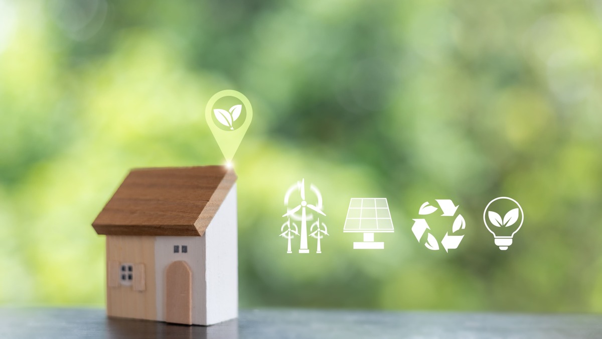 木製ミニチュアハウスの横に風力・太陽光・リサイクル・省エネ電球のアイコンが並ぶ画像。家庭における省エネと再生可能エネルギーの活用を示すイメージ画像。