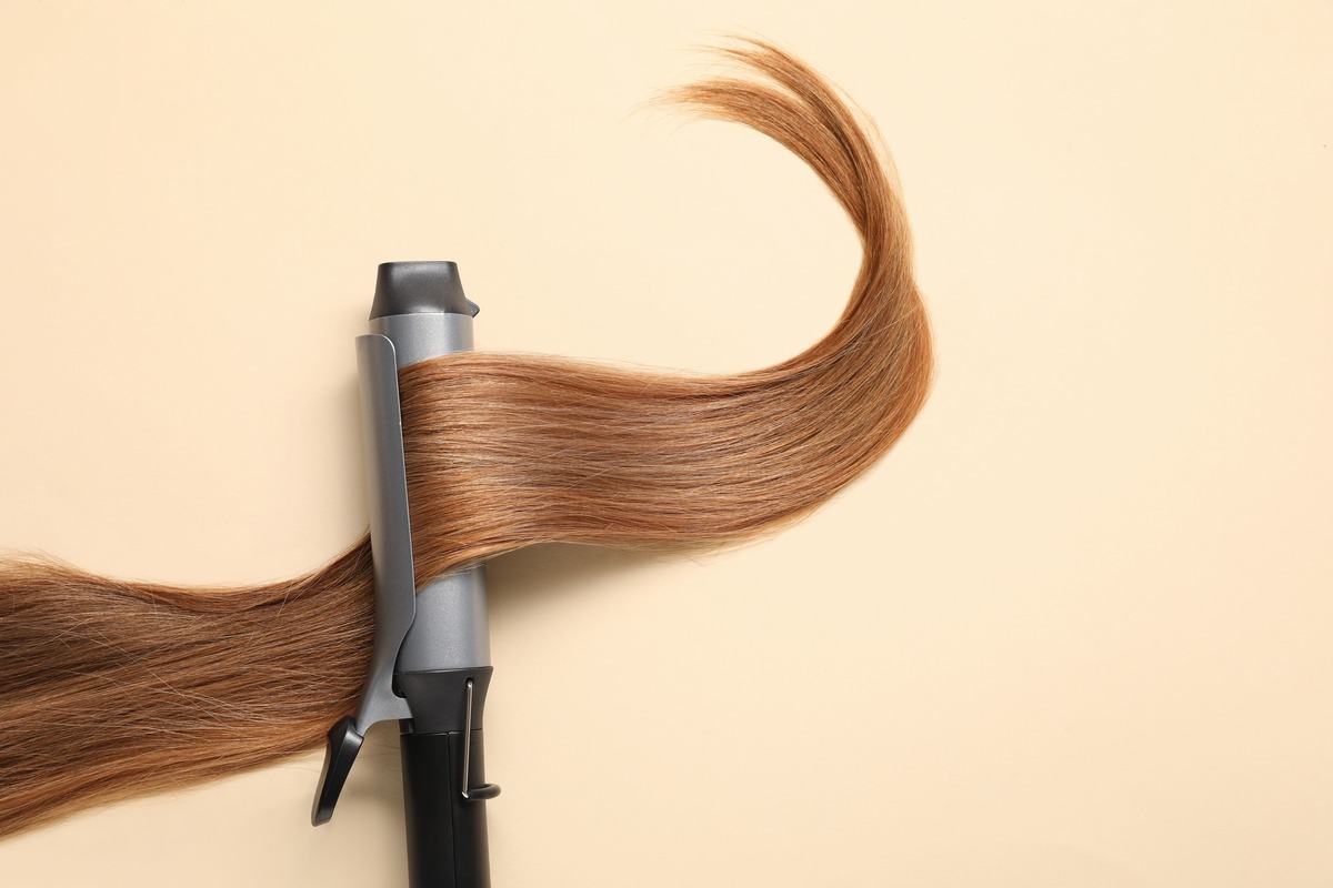 コテで茶色の髪の毛を巻いている様子をクローズアップした写真。ヘアアイロンの実際の使用シーンを示すイメージ。