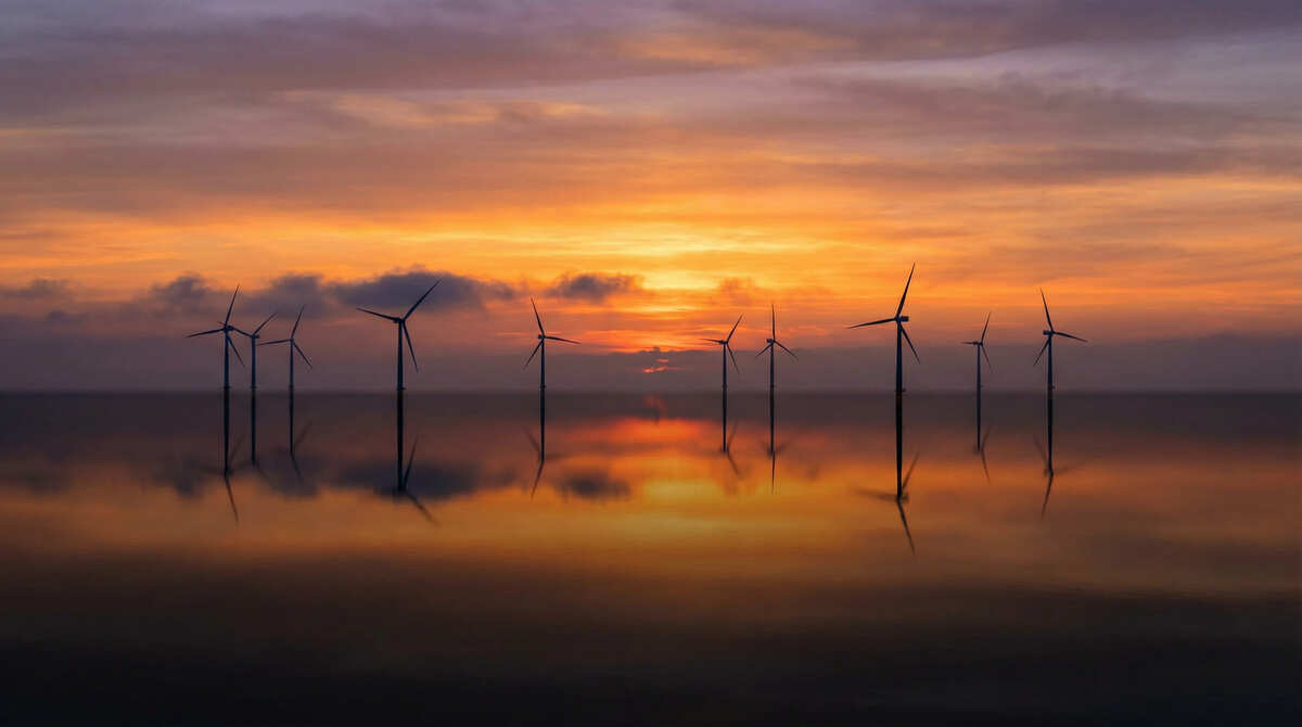 夕焼けの空と海面に映り込む洋上風力発電タービンのシルエット。