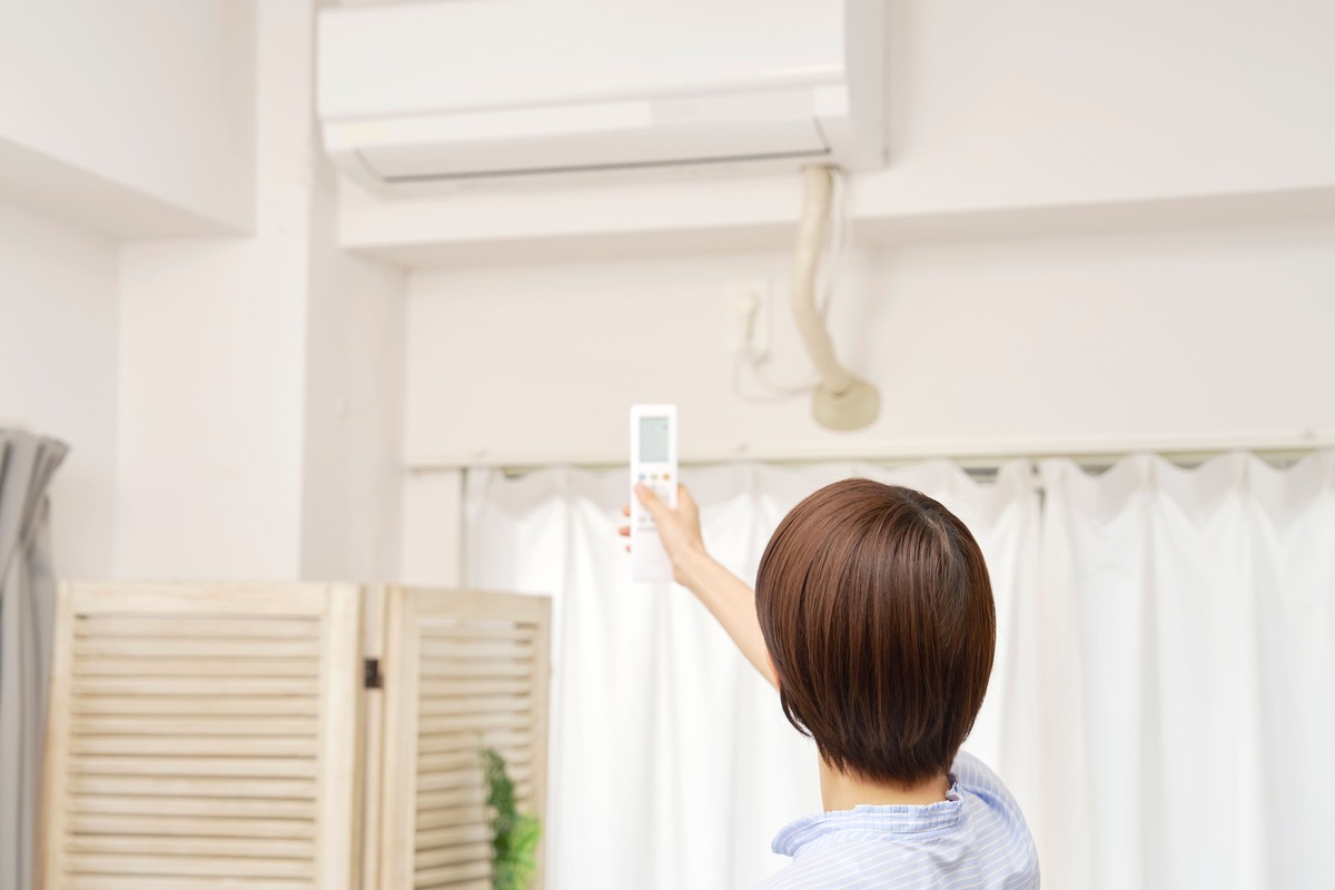 エアコンにリモコンを向ける女性の後ろ姿。節電を意識したエアコンの適切な使い方を示すイメージ。