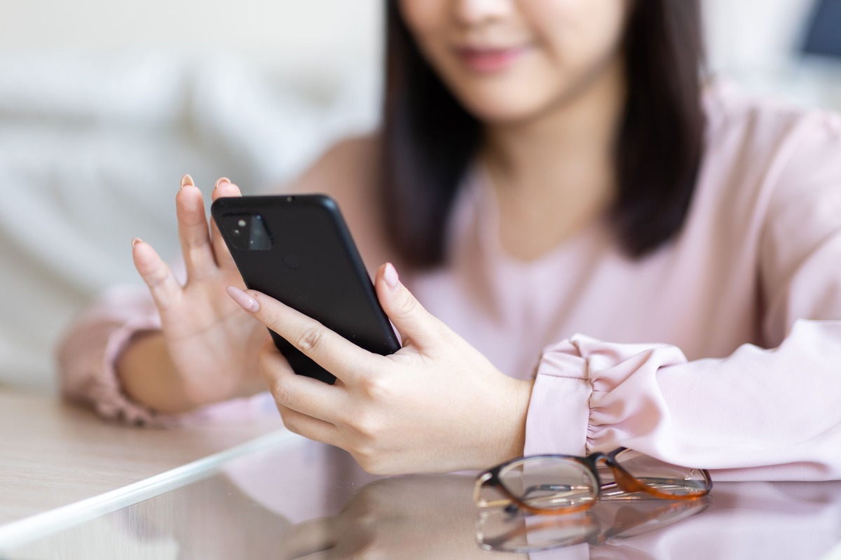 スマートフォンを操作する若い女性の手元のクローズアップ。通信費などの固定費削減を示すイメージ。