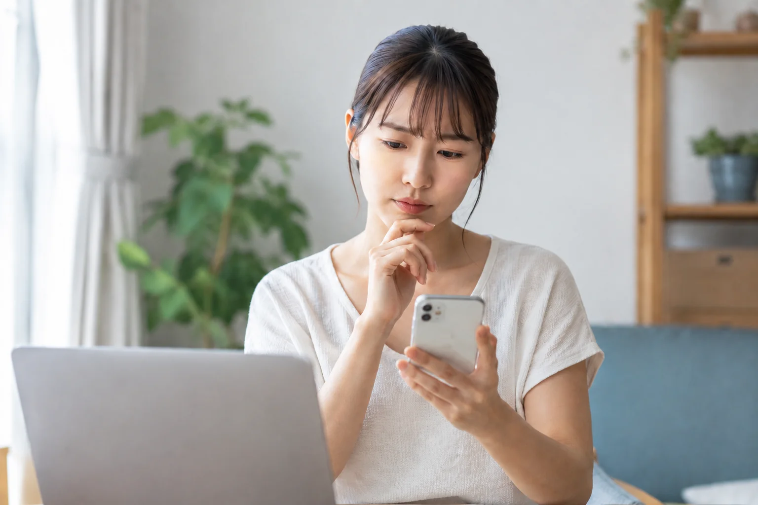 スマートフォンを見ながら考え込む女性。電気代の明細を確認して「なぜ高いのか」を考え込むイメージ写真。